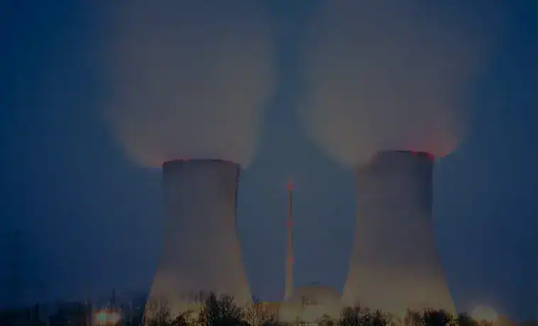 Cooling towers emitting steam at a nuclear power plant during nighttime.