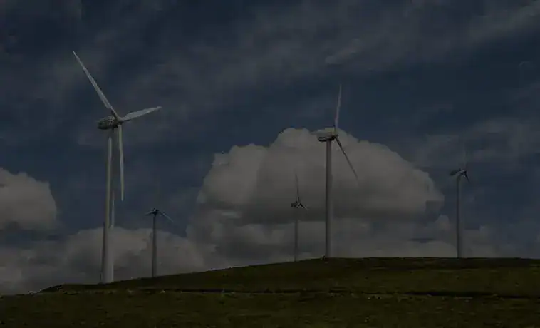 Wind turbines generating renewable energy on a hilltop under a cloudy sky.